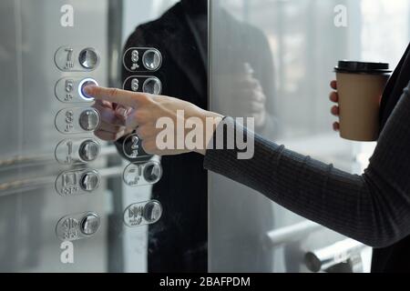 Main de la jeune femme d'affaires avec boisson bouton-poussoir à l'intérieur de l'ascenseur tout en retournant au bureau au cinquième étage à la pause café Banque D'Images