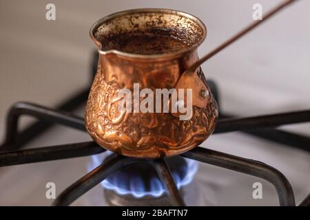 Cafetière turque en cuivre avec un café bouillante à l'intérieur debout sur la cuisinière Banque D'Images