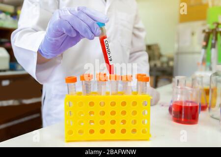 Microbiologiste avec un tube d'échantillon biologique contaminé par le coronavirus avec l'étiquette Covid-19 dans le laboratoire. Banque D'Images