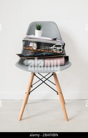 Chaise en plastique grise avec une pile de fournitures de bureau ou de trucs de designer d'intérieur avec petit pot de fleurs sur son dessus debout isolément par le mur blanc Banque D'Images