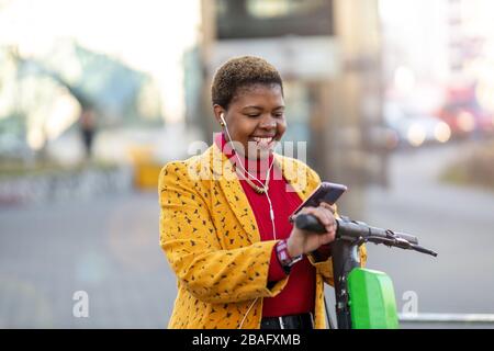 Jeune femme avec scooter électrique de vérifier son smartphone Banque D'Images