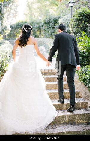 La mariée et le marié posent sur la main. Au coucher du soleil, sur le lieu du mariage. La mariée tient une fleur de mariée dans sa main. Banque D'Images