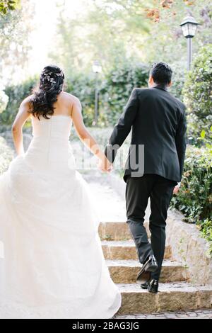 La mariée et le marié posent sur la main. Au coucher du soleil, sur le lieu du mariage. La mariée tient une fleur de mariée dans sa main. Banque D'Images