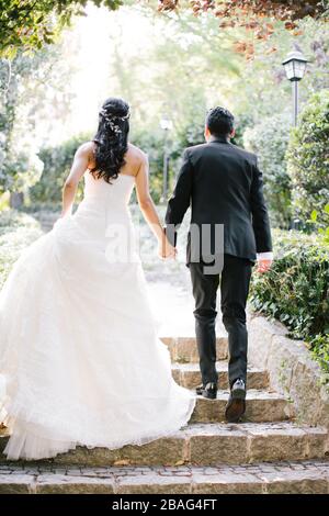 La mariée et le marié posent sur la main. Au coucher du soleil, sur le lieu du mariage. La mariée tient une fleur de mariée dans sa main. Banque D'Images