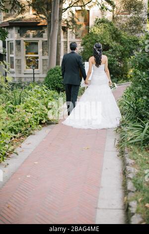 La mariée et le marié posent sur la main. Au coucher du soleil, sur le lieu du mariage. La mariée tient une fleur de mariée dans sa main. Banque D'Images