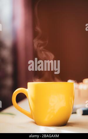 Tasse jaune avec boisson chaude en streaming à thé sur table avec fond rose foncé dans une belle lumière du matin Banque D'Images