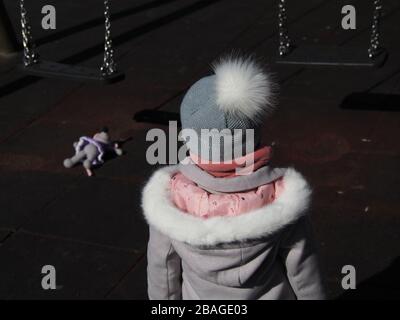 Une jeune fille debout sur une aire de jeux pour enfants regarde un swing une souris jouet posée sur le sol Banque D'Images