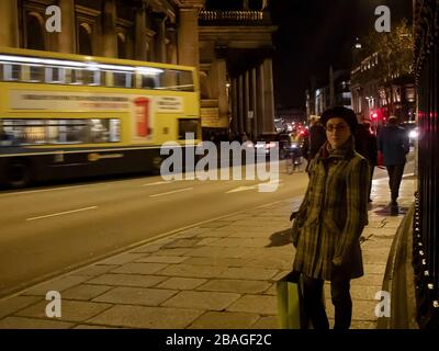 Une jeune dame se tient sur le sentier en face du siège de la Banque d'Irlande à Dublin pendant l'heure de roussouh du soir Banque D'Images