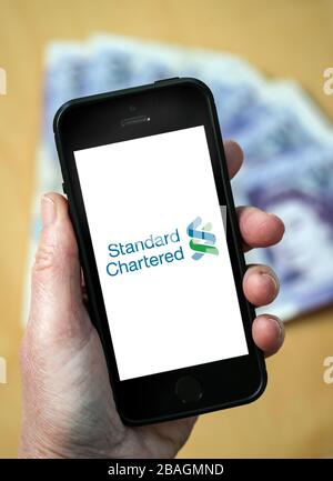 Une femme regardant le logo Standard Chartered Bank sur un téléphone mobile. (Usage éditorial uniquement) Banque D'Images