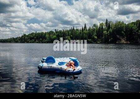 Jeune enfant ponçant sur un radeau flottant sur la rivière dans le nord de l'ontario Banque D'Images