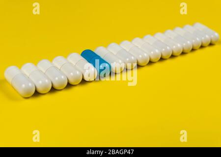 une capsule de pilule bleue parmi les pilules blanches sur fond jaune Banque D'Images