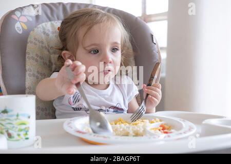 Petite fille mangeant seule dans la chaise près de la table. Banque D'Images