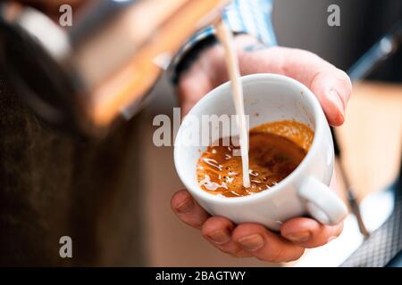 Fermez les mains du Barista Man en versant du lait cuit à la vapeur dans du café maison. Faire de beaux Latte Art. Rester concept à la maison. Banque D'Images