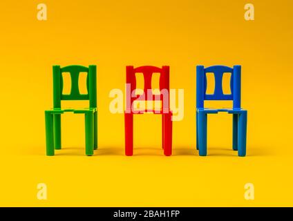trois chaises en plastique de différentes couleurs sur fond jaune Banque D'Images