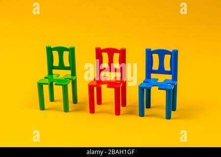 trois chaises en plastique de différentes couleurs sur fond jaune Banque D'Images