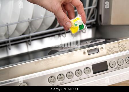 Fermeture de la languette au lave-vaisselle. Machine à lave-vaisselle intégrée pleine charge. Femme tenant la tablette à lessive au lave-vaisselle. Banque D'Images