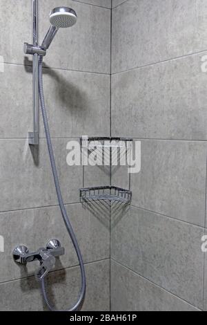 Cabine de douche avec carrelage gris. Robinet, tuyau et pomme de douche, étagère d'angle en tiges métalliques. Banque D'Images