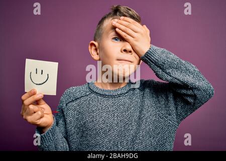 Jeune enfant caucasien montrant le visage souriant sur une note papier comme un message heureux souligné avec la main sur la tête, choqué avec la honte et le visage surprise, angr Banque D'Images