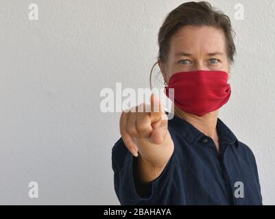Une femme caucasienne pose pour l'appareil photo avec son masque facial (fabriqué à partir d'une vieille pochette de t-shirt) pendant l'épidémie de corona-virus 2019/20. Banque D'Images