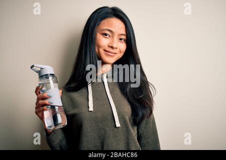 Jeune sportif chinois qui tient une bouteille d'eau sur fond blanc isolé avec un visage heureux debout et souriant avec un smi confiant Banque D'Images