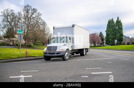 Petit engin de semi-camion blanc à capot compact avec remorque à cube transportant du fret commercial conduisant dans la rue de la ville urbaine au printemps avec Banque D'Images