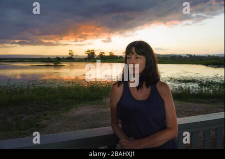 Woman, au coucher du soleil, se penchant sur l'affichage de rail de la plate-forme, au milieux humides du Saint-Laurent, près de Mackay, Queensland, Australie. Banque D'Images