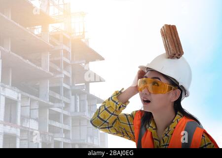 La brique de blocage de bâton est tombée sur la jeune femme ingénieur d'Asie tête sur le casque travailleur sur fond blanc, la sécurité de construction de zone premier concept Banque D'Images