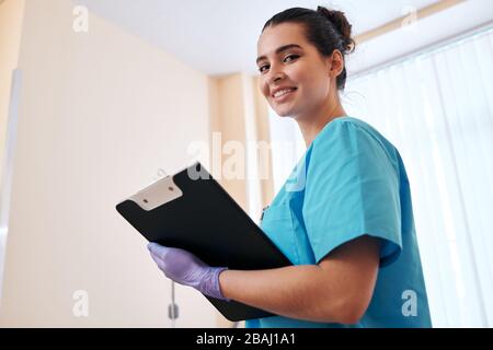 Portrait d'une infirmière souriante dans des gants chirurgicaux prenant des notes sur la carte médicale lors des visites à l'hôpital Banque D'Images