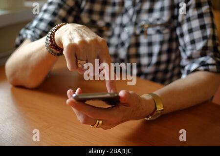 Une femme senior s'assoit à la table tout en utilisant le concept de smartphone toujours en ligne, connexion, achats en ligne, auto-isolation, technologie moderne pour les personnes âgées Banque D'Images