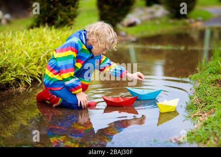 Enfant jouant avec paper boat en flaque. Les enfants jouent en plein air pluie d'automne. Le temps pluvieux de l'automne de l'activité en plein air pour les jeunes enfants. Kid jumping dans la boue Banque D'Images