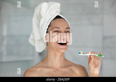 Tête de rire de la femme avec une serviette sur la tête tenant la brosse à dents Banque D'Images
