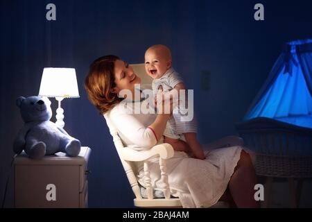 La mère et l'enfant de lire un livre dans une chambre sombre. Maman et enfant à lire les livres avant de le mettre au lit. Famille dans la soirée. Chambre d'enfant intérieur avec une lampe de nuit Banque D'Images