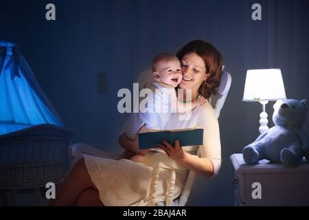 La mère et l'enfant de lire un livre dans une chambre sombre. Maman et enfant à lire les livres avant de le mettre au lit. Famille dans la soirée. Chambre d'enfant intérieur avec une lampe de nuit Banque D'Images