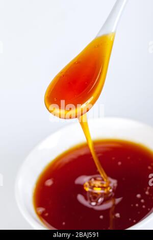 le miel s'écoule de la cuillère en céramique à la cuvette en céramique Banque D'Images