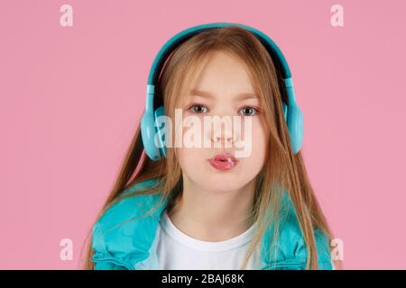 Une petite fille avec casque explose la gomme à mâcher rose sur un fond rose. Banque D'Images