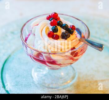 verre de crème fouettée blanche pure avec sirop doux et baies rouges juteuses Banque D'Images