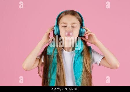 Une petite fille avec casque explose la gomme à mâcher rose sur un fond rose. Banque D'Images