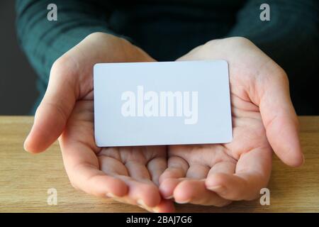 Une carte rectangulaire blanche se trouve dans les paumes ouvertes d'une fille dans un pull bleu. Maquette pour la conception, place pour le texte, espace de copie. Banque D'Images