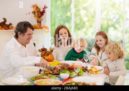 Famille avec enfants mangeant le dîner de Thanksgiving. dinde rôtie et tarte à la citrouille sur la table à manger avec décoration d'automne. Les parents et les enfants ayant des fpris Banque D'Images