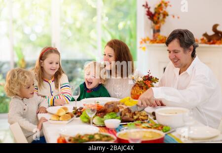 Famille avec enfants mangeant le dîner de Thanksgiving. dinde rôtie et tarte à la citrouille sur la table à manger avec décoration d'automne. Les parents et les enfants ayant des fpris Banque D'Images