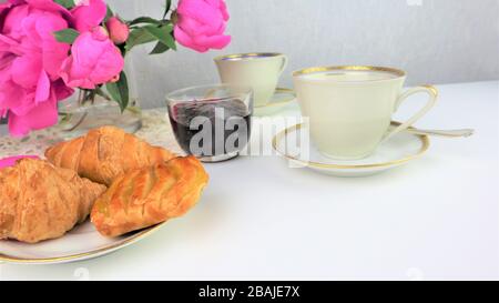 Le petit-déjeuner avec deux tasses de café et croissants, bouquet de fleurs roses pivoines Banque D'Images