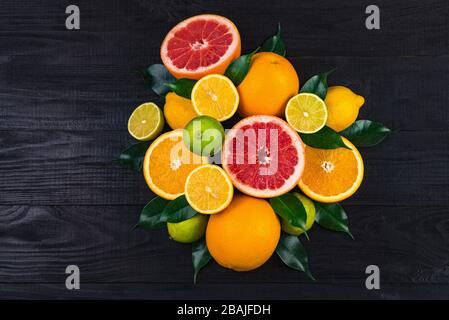 de nombreux agrumes, des pamplemousses, des citrons, des oranges, des limes avec des feuilles vertes se trouvent sur une table en bois brun. immense montagne de fruits. un bouquet de vitamines. ba Banque D'Images