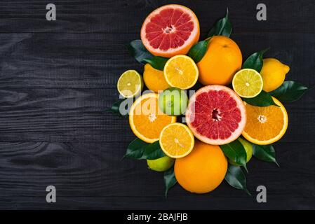 de nombreux agrumes, des pamplemousses, des citrons, des oranges, des limes avec des feuilles vertes se trouvent sur une table en bois brun. immense montagne de fruits. un bouquet de vitamines. ba Banque D'Images