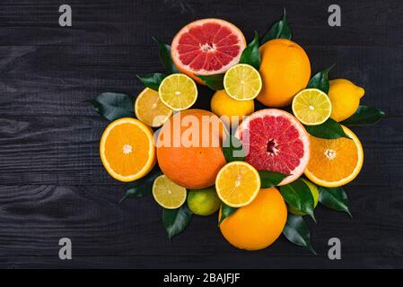 de nombreux agrumes, demi-pamplemousses, citrons, oranges, limes à feuilles vertes se trouvent sur une table en bois brun. immense montagne de fruits. un bouquet de vitami Banque D'Images