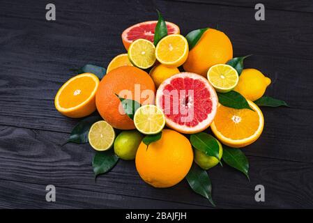 agrumes, demi-pamplemousses, citrons, oranges, limes à feuilles vertes se trouvent sur une table en bois brun. immense montagne de fruits. un bouquet de vitamines. ba Banque D'Images