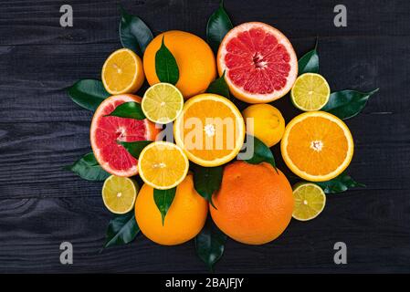 fruits, demi-pamplemousses, citrons, oranges, limes à feuilles vertes se trouvent sur une table en bois marron. arrière-plan. vue de dessus Banque D'Images