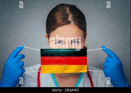 Coronavirus en Allemagne, Deutschland Female Doctor Portrait HOLD protéger le masque médical chirurgical visage avec drapeau national de l'Allemagne. Maladie, virus Covid-19 Banque D'Images