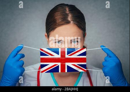 Coronavirus au Royaume-Uni, en Grande-Bretagne, en Angleterre médecin féminin Portrait tenir protéger visage masque médical chirurgical avec drapeau national du Royaume-Uni Banque D'Images