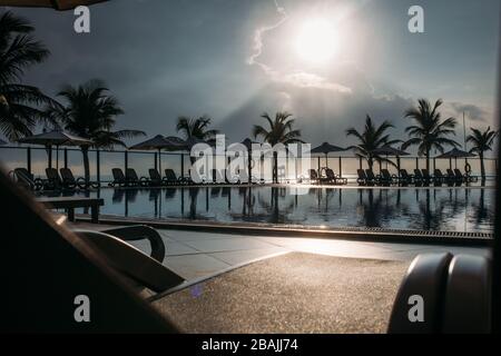 Piscine, palmiers autour, reflet de palmiers dans la piscine, aube avec un beau ciel nuageux. Une zone vide avec de nombreux transats, le soleil pas Banque D'Images