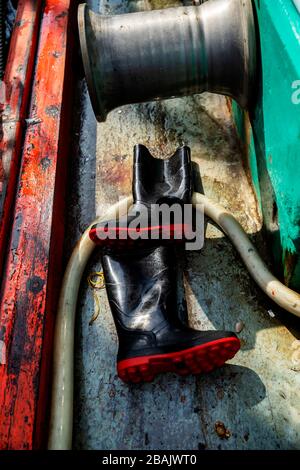 Bottes en caoutchouc noir pêcheur avec semelle rouge sur le sol du bateau Banque D'Images